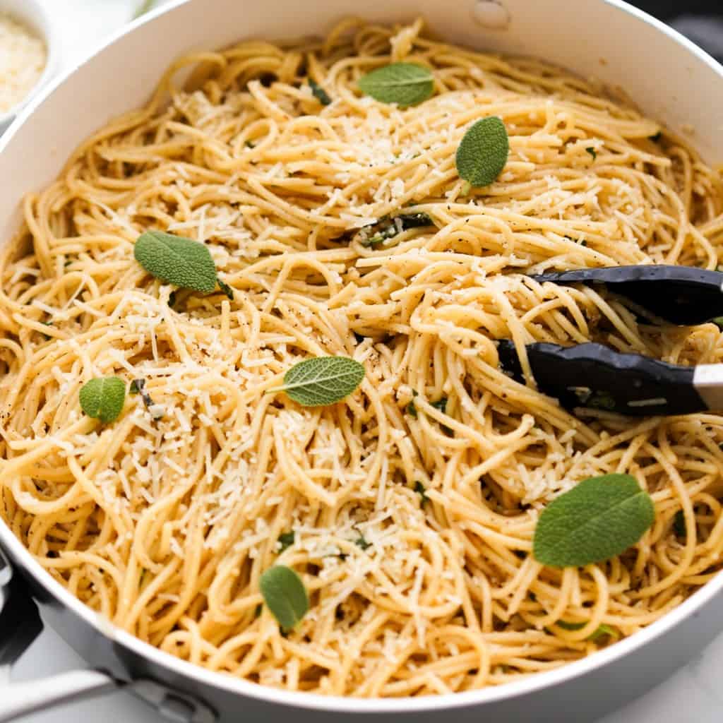 A pair of tongs in a large pot of brown butter sage pasta