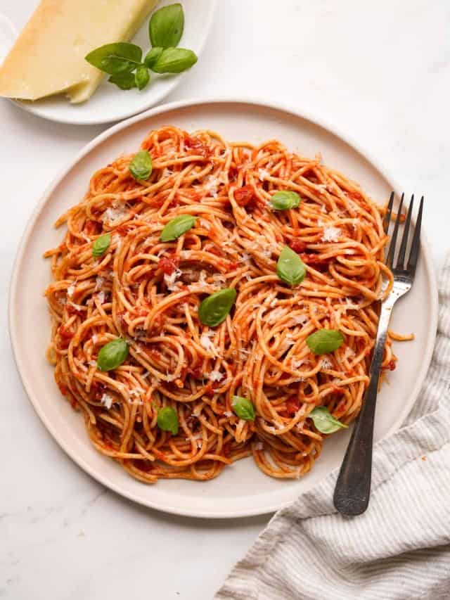 A plate of pasta pomodoro with parmesan cheese and fresh basil leaves in the background