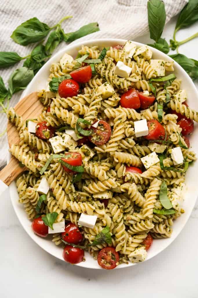 A large oval plate loaded with pesto pasta salad