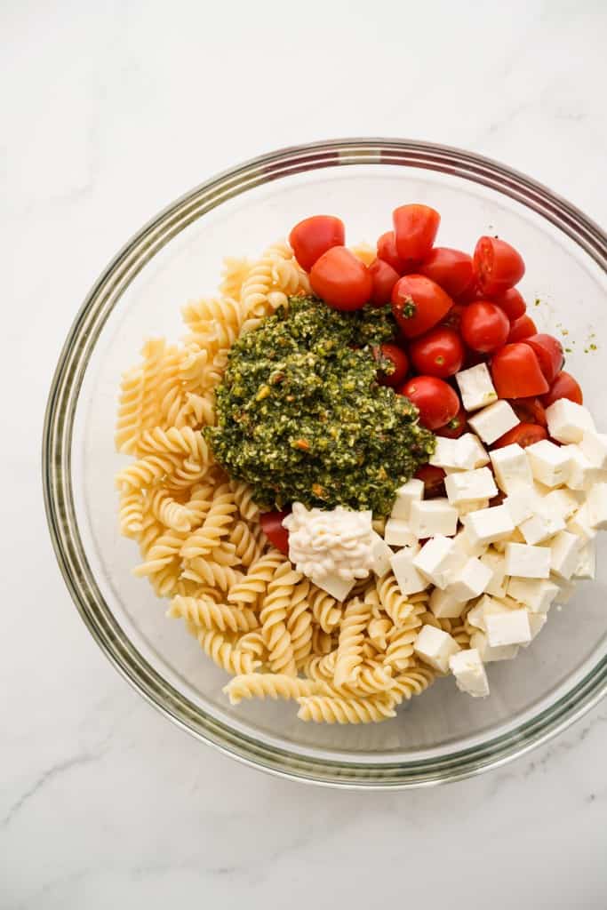 Spiral pasta, halved cherry tomatoes, cubed feta, mayo and pesto in a large mixing bowl.