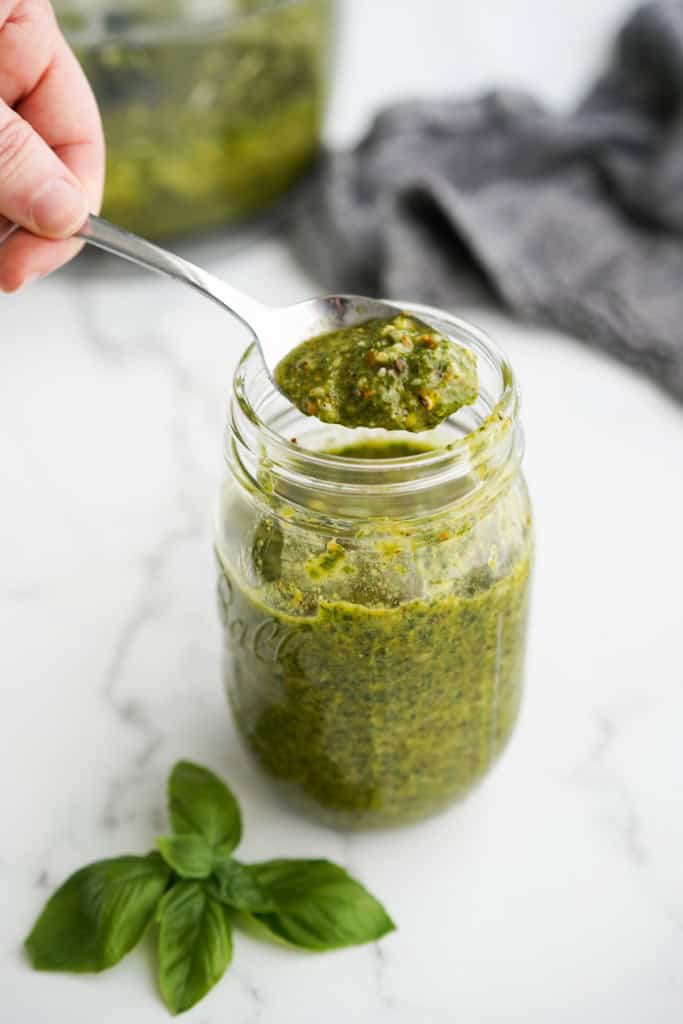 Using a spoon to scoop out some pistachio pesto from a jar