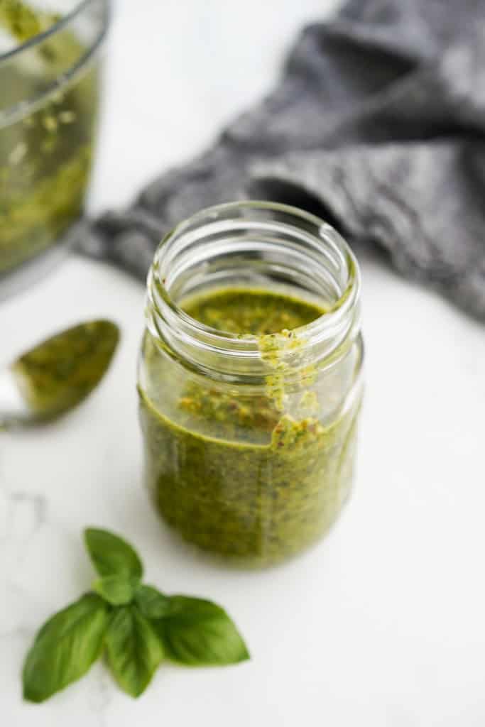A jar of pistachio pesto with a spoon in the background