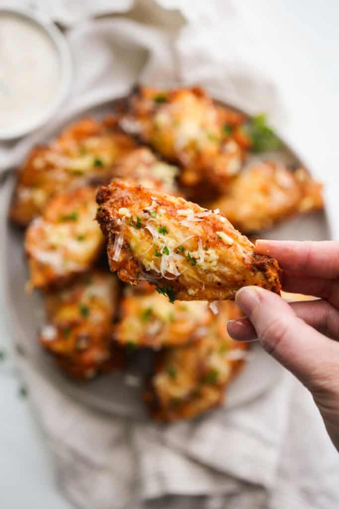 Picking up a winglette from a plate of crispy baked wings
