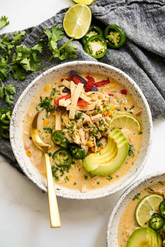 A bowl of chunky white chicken chili with avocados, and tortilla chips on top