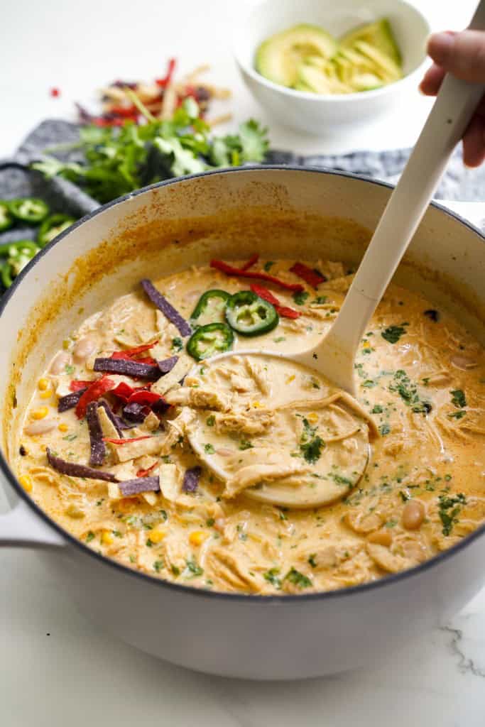 a large pot of white chicken chili soup and a ladle scooping some of it out