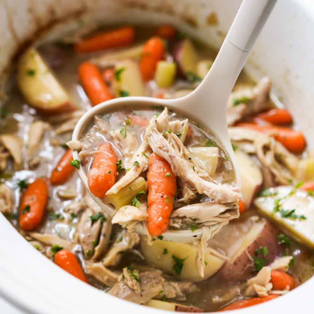 Using a ladel to scoop out a large spoonful of chunky chicken stew with carrots and potatoes