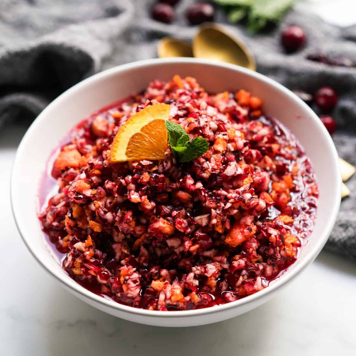 A bowl of chunky cranberry relish topped with a wedge of orange and mint leaves