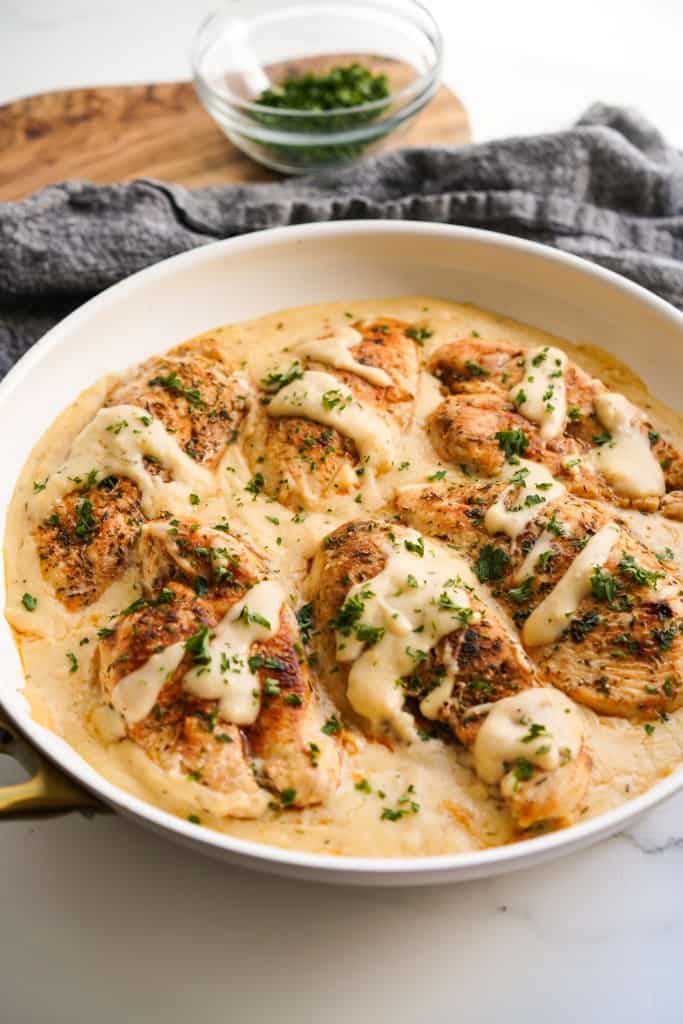 A skillet of garlic herb chicken smothered in creamy white sauce.