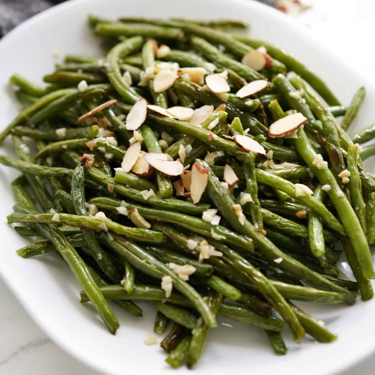 A plate of oven baked green beans tossed in garlic and topped with almonds