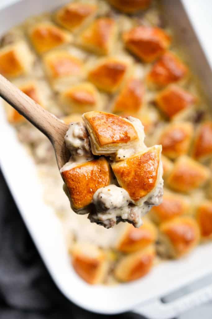 Listing up a spoonful of thick sausage gravy topped with bite sized pieces of golden brown biscuits
