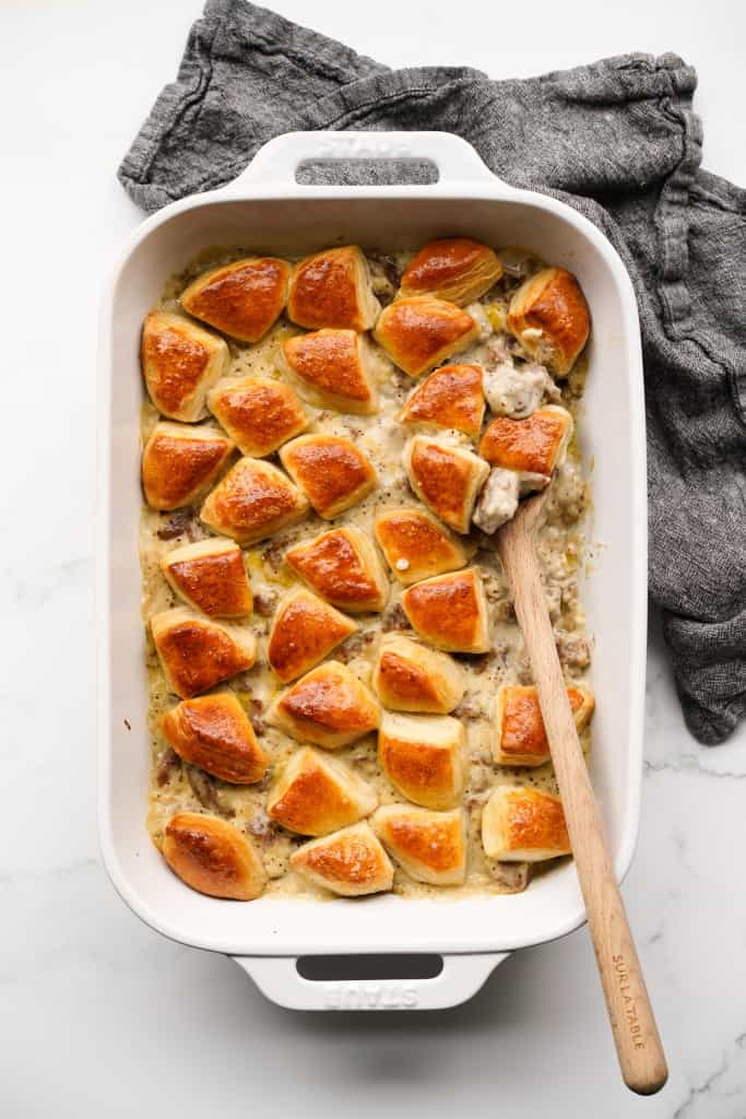 A large casserole dish of biscuit and gravy casserole, with a wooden spoon digging into it