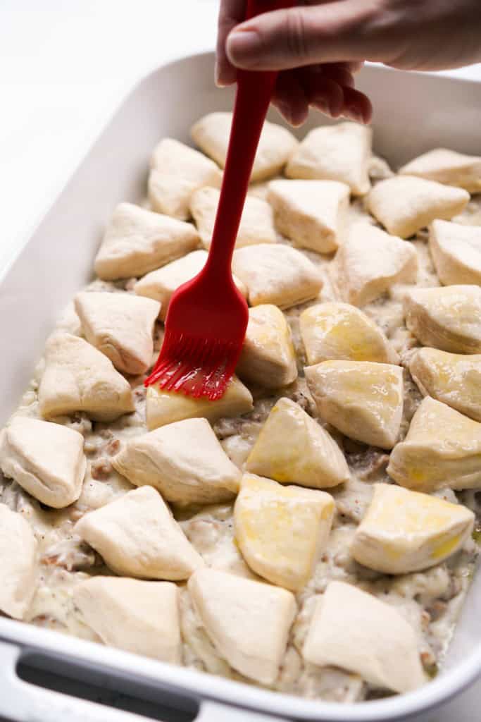 Brushing the tops of biscuits sitting on the sausage gravy in casserole dish with egg wash