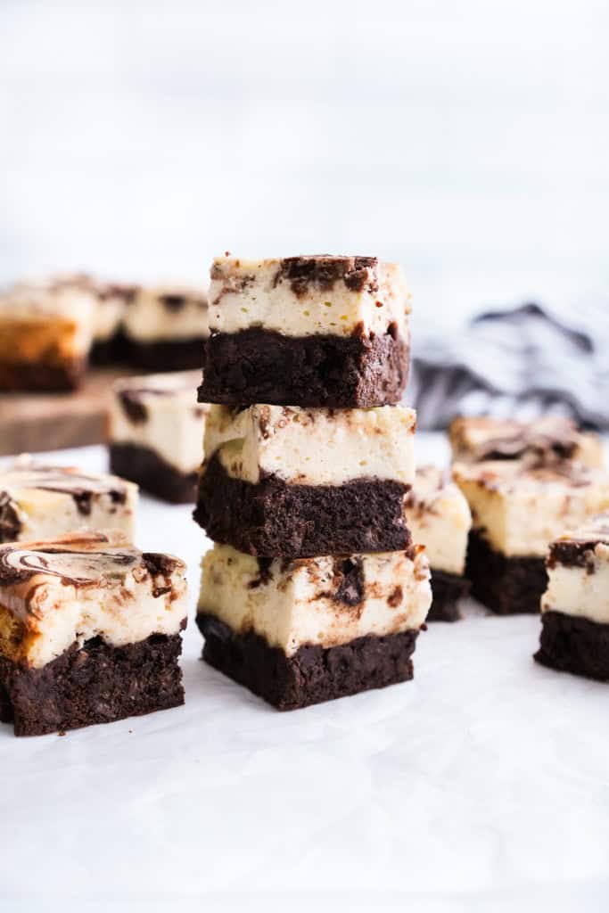A stack of three pieces of cheesecake brownies with more scattered in the background