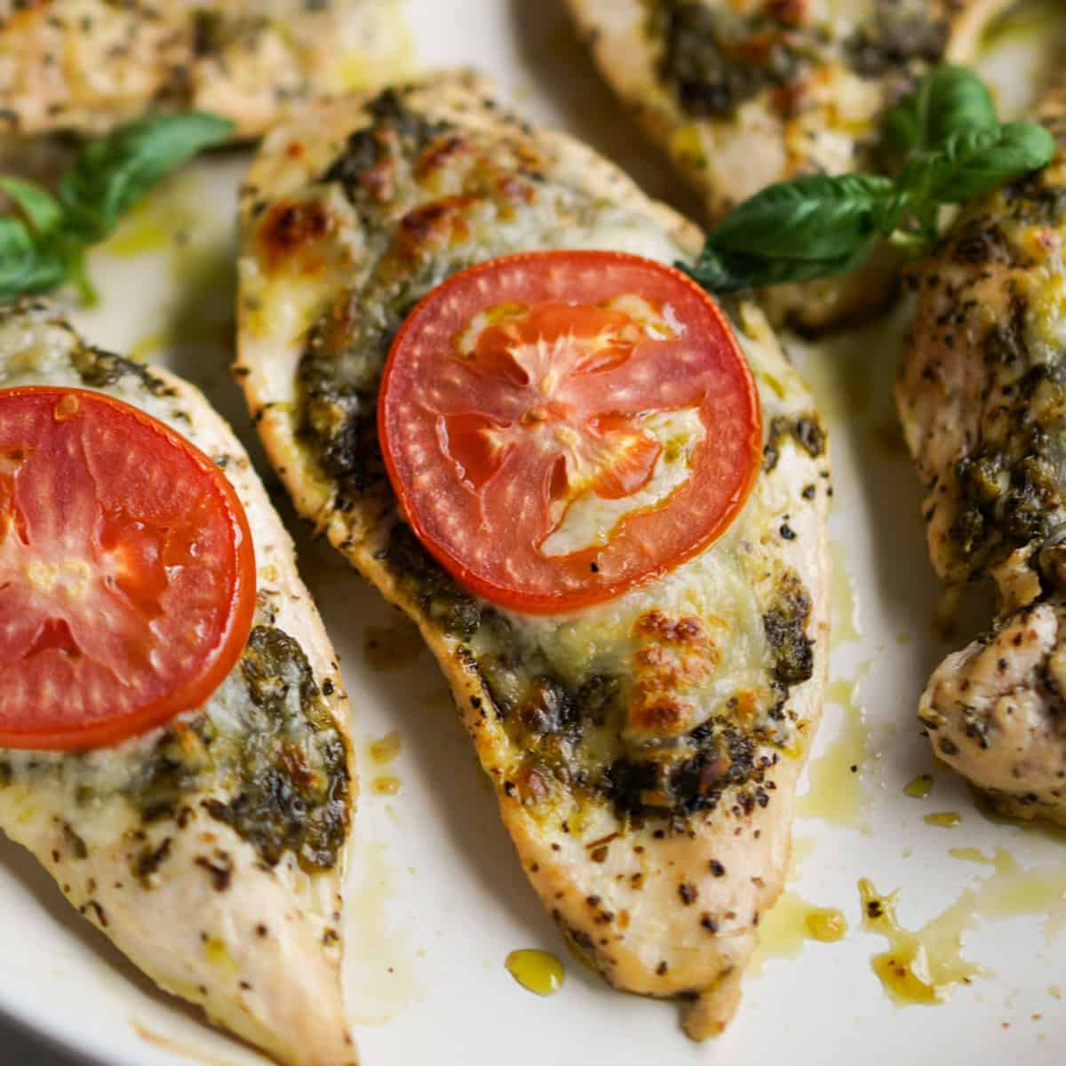 A thin slice of chicken breast topped with pesto, melted mozzarella cheese and sliced tomato
