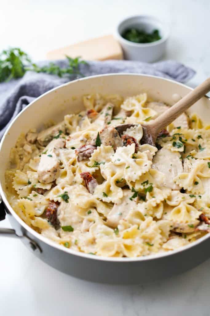 A large pot of bow tie pasta tossed in creamy sauce, chicken and sundried tomatoes