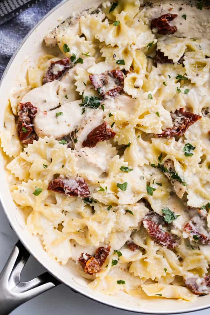 Close up of cream sundried tomato pasta tossed along side sliced chicken breast 
