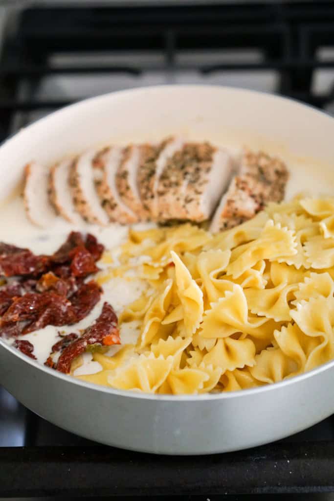 Adding pasta, sliced chicken and sun dried tomatoes