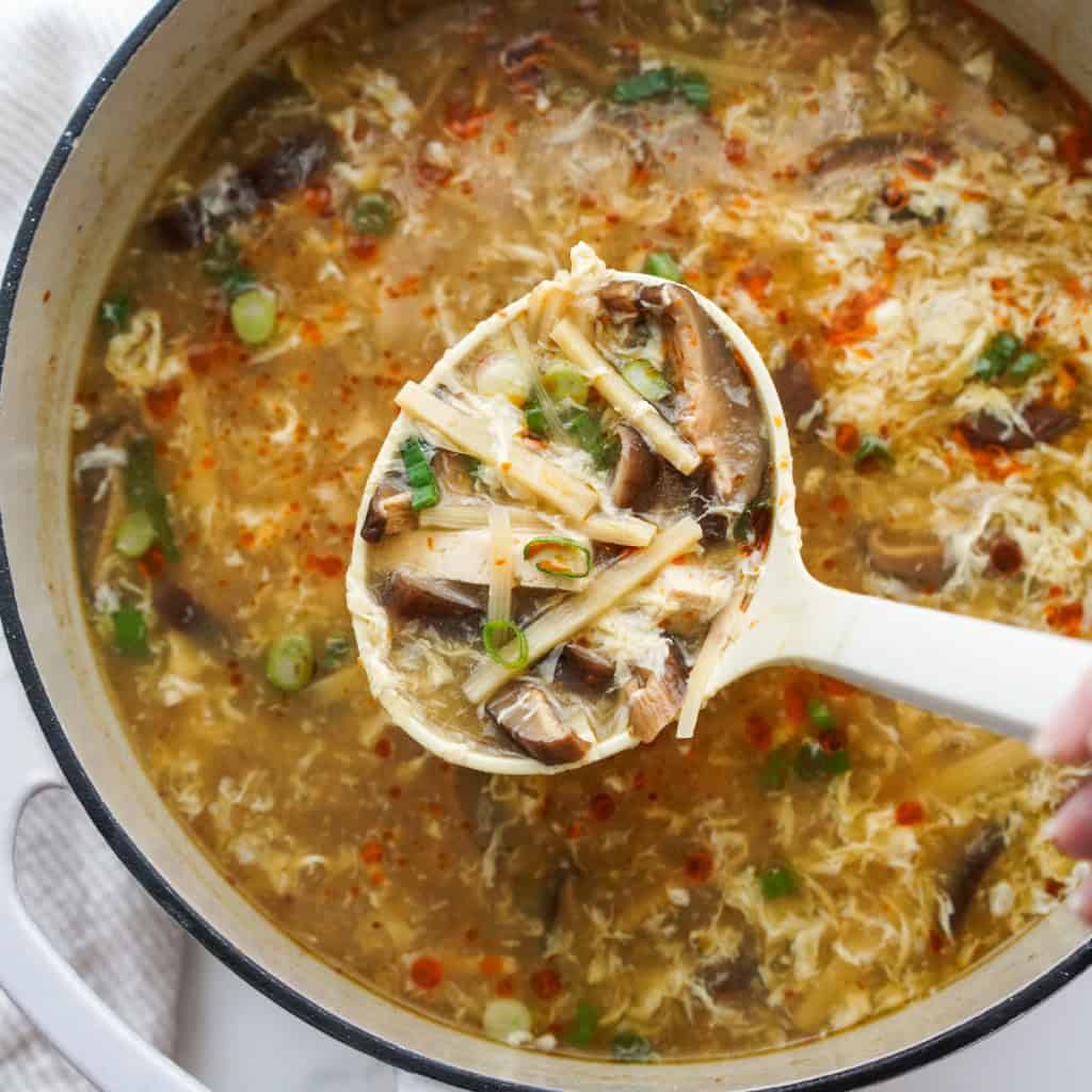 Picking up tofu, bamboo shoots and mushrooms from a large pot of hot and sour soup