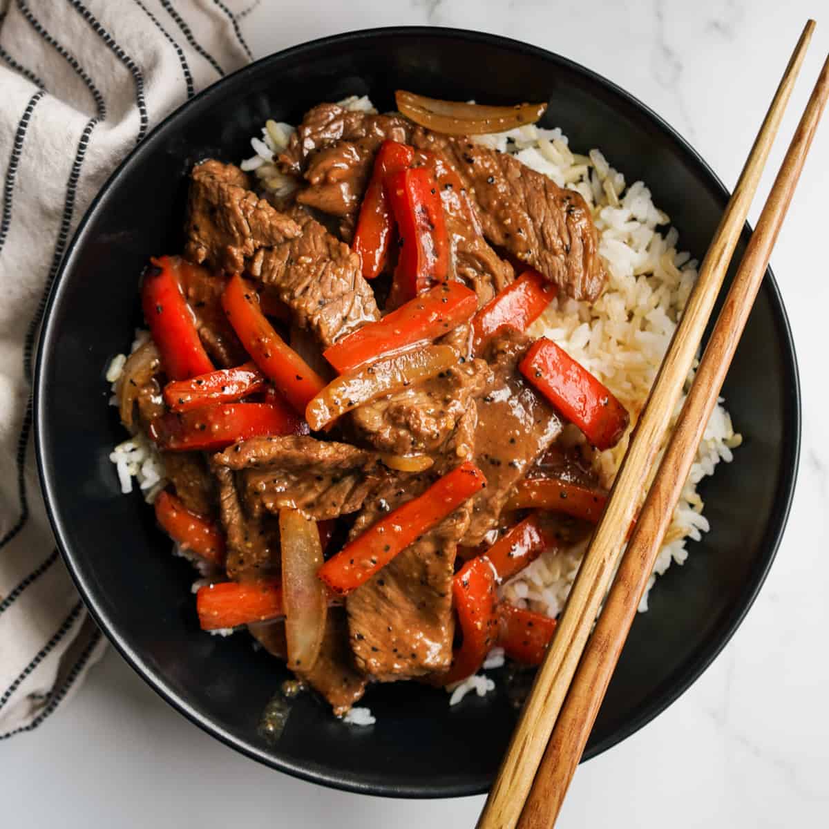 A round bowl filled with rice and black pepper beef and bell peppers