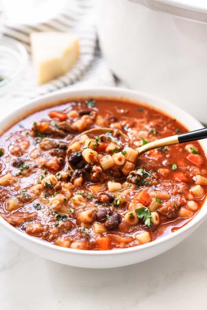 Spooning out a spoonful of pasta, ground beef and beans from a bowl of pasta fagioli soup