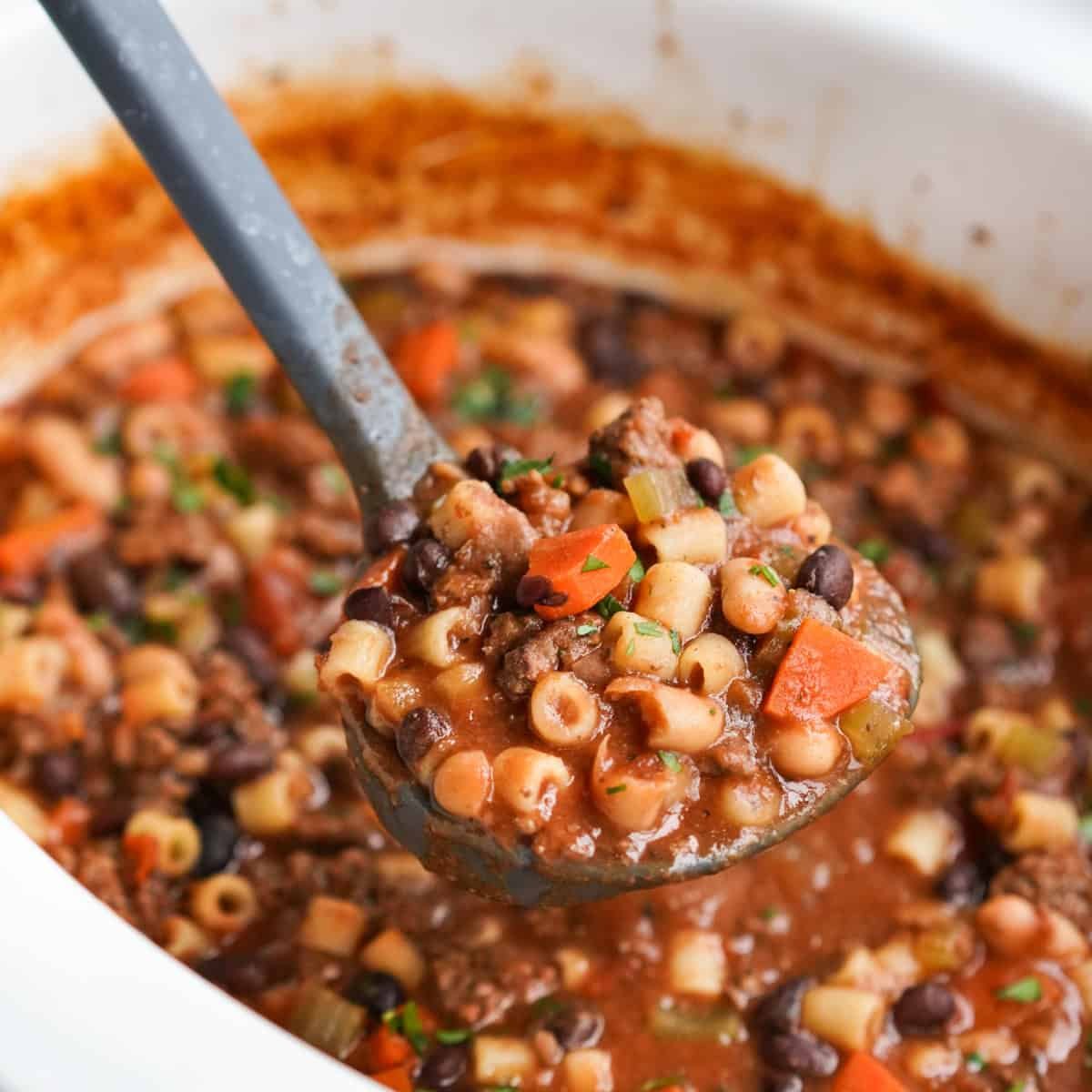 Lifting up a scoop of pasta fagioli soup from the crockpot