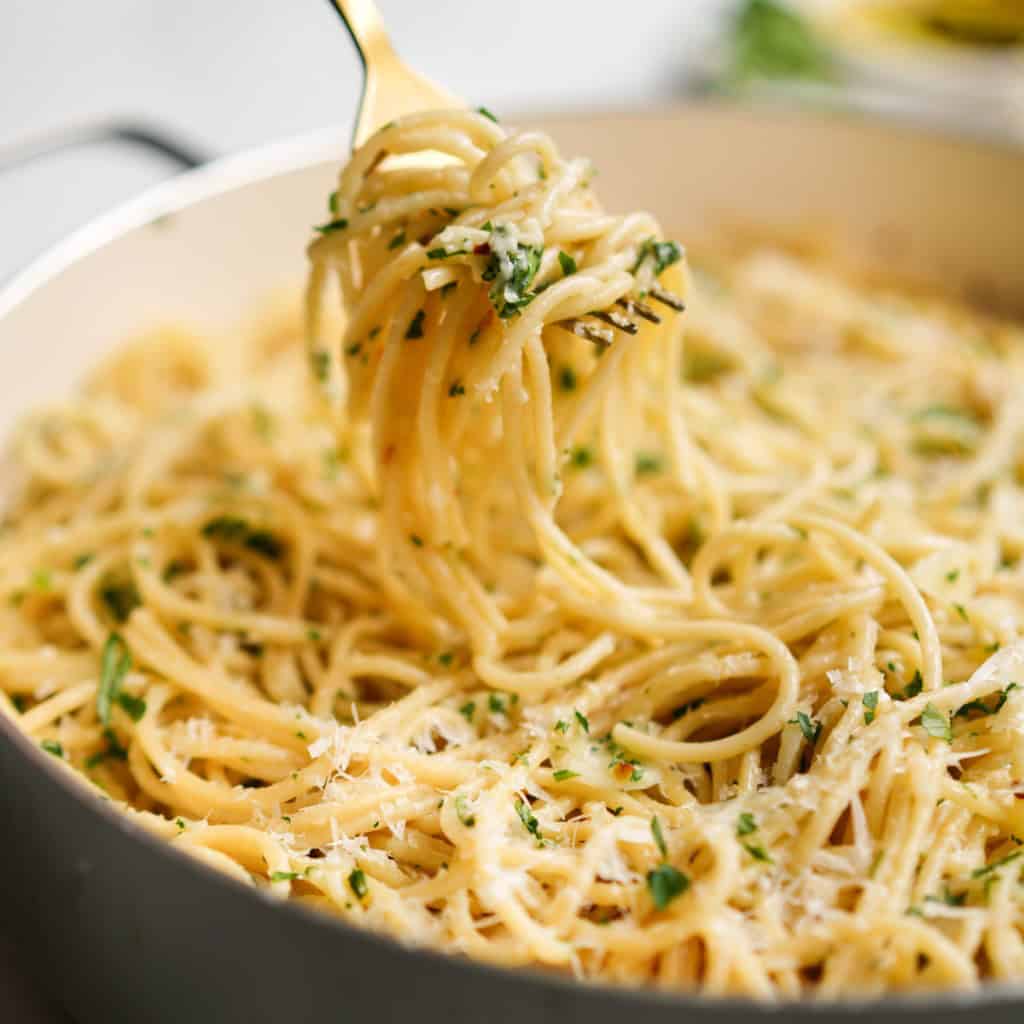 Lifting up spaghetti tossed in garlic and olive oil with a fork