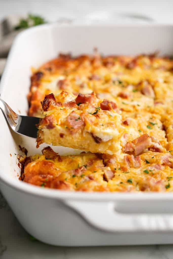 Lifting up a slice of egg casserole loaded with potatoes, ham and cheese