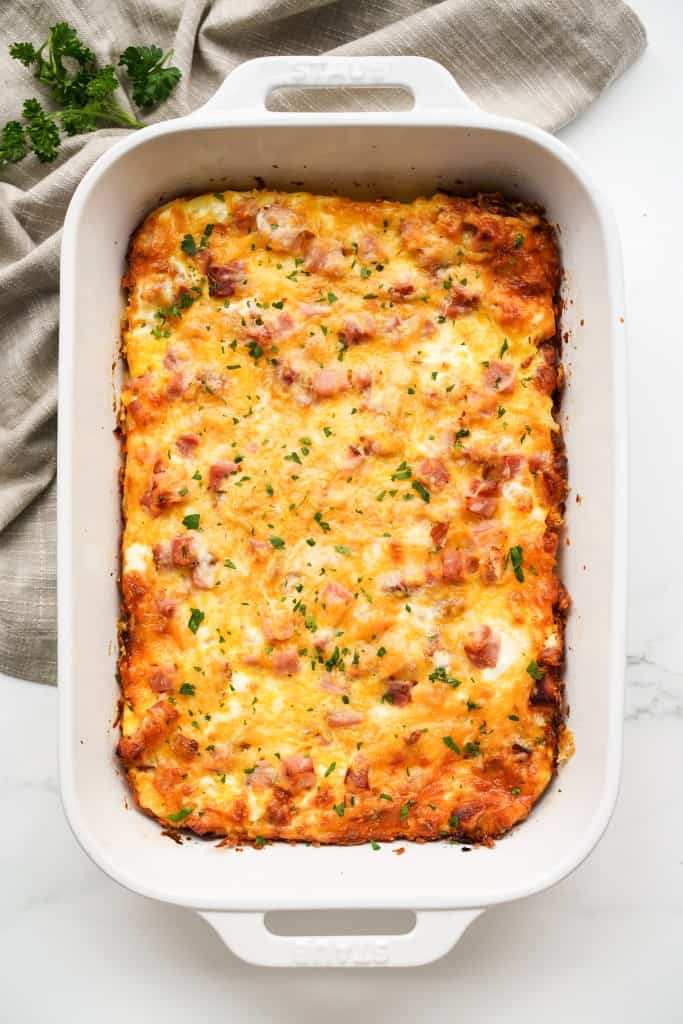 A large rectangular casserole dish with hashbrown egg bake topped with ham and cheese