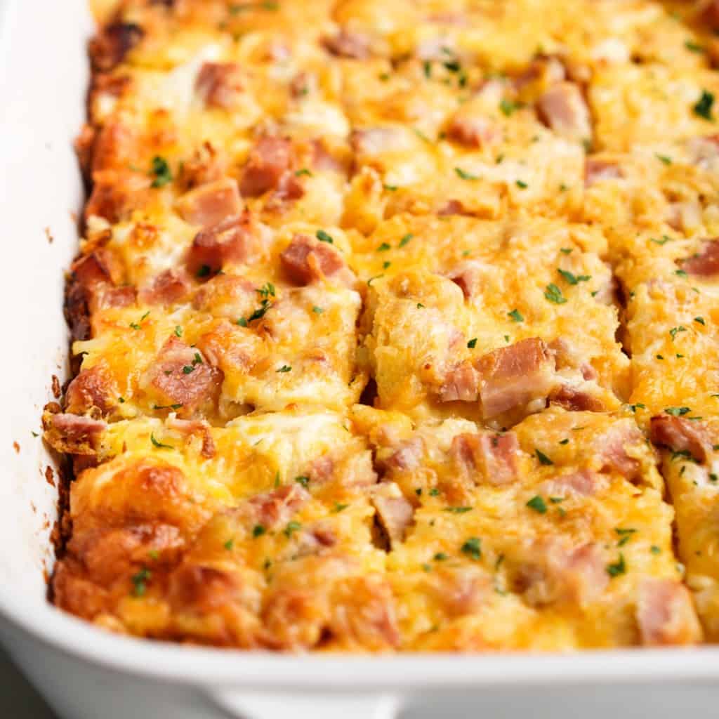 Hashbrown egg casserole topped with ham and cheese sliced into squares in a casserole dish