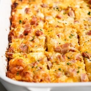 Hashbrown egg casserole topped with ham and cheese sliced into squares in a casserole dish