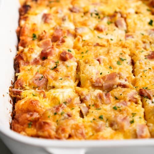 Hashbrown egg casserole topped with ham and cheese sliced into squares in a casserole dish