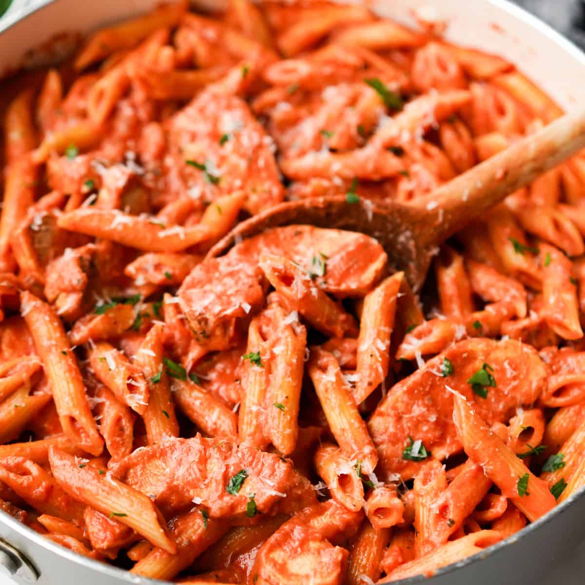 A wooden spoon stirring a skillet loaded with chicken penne alla vodka