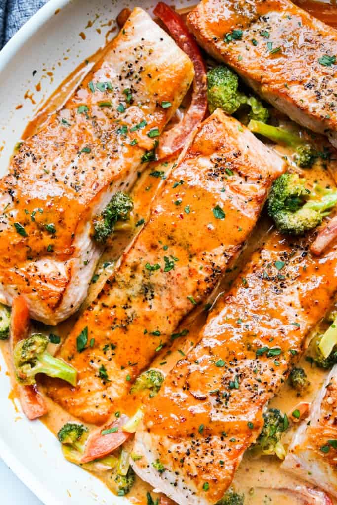 Closeup of salmon fillets covered in creamy thai red curry sauce, along with broccoli and bell peppers.