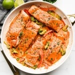 A large skillet with salmon fillets coated in red curry sauce, with broccoli and red bell peppers in the sauce.