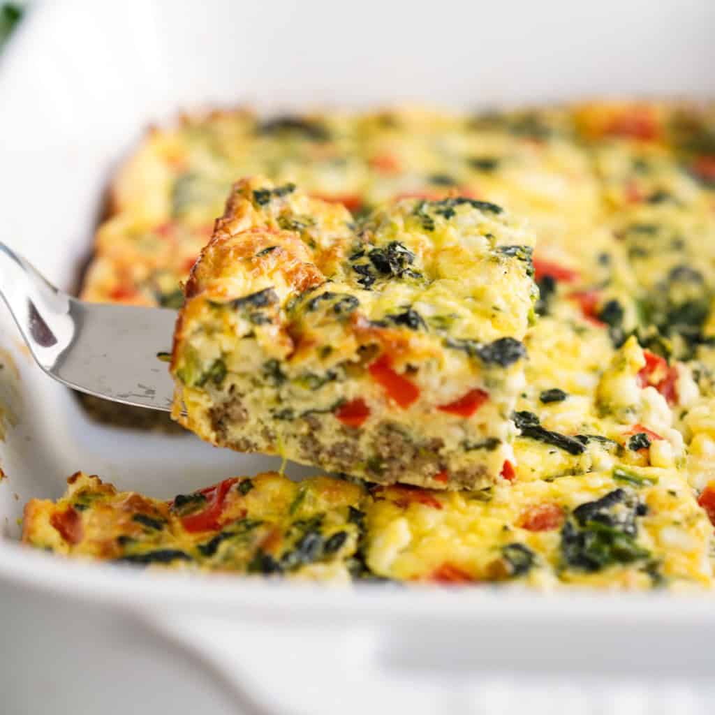 LIfting up a slice of cottage cheese egg bake with spinach, peppers and crumbled sausage