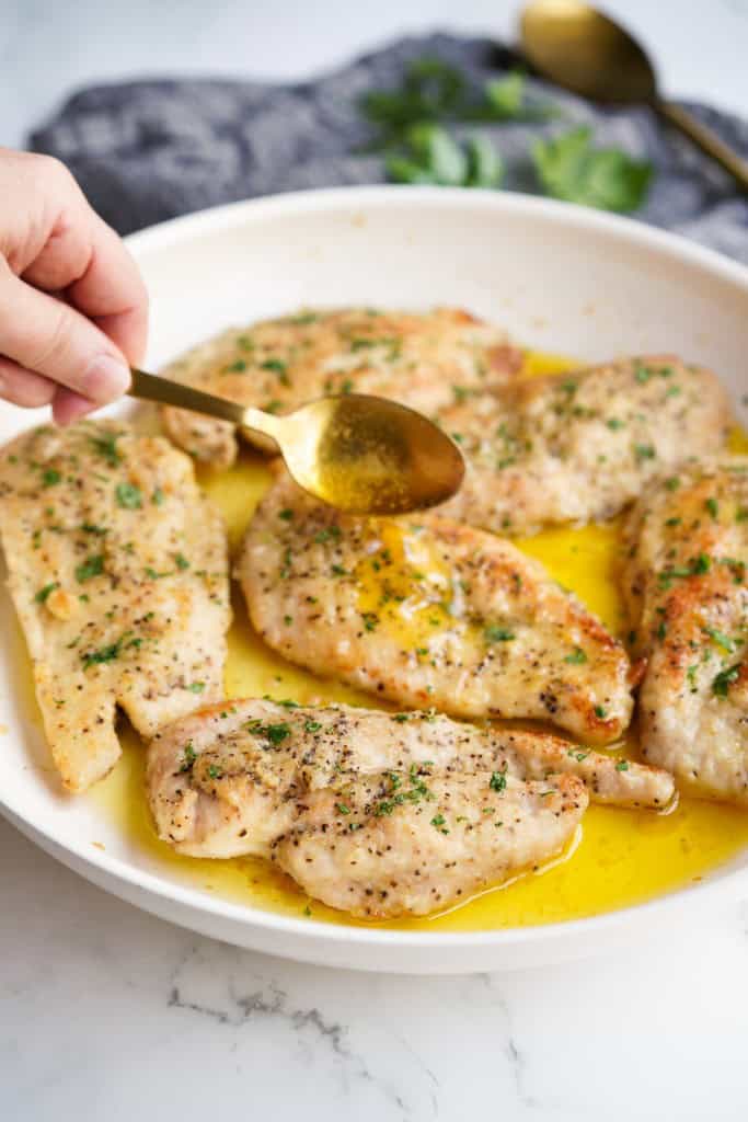 Spooning melted butter over seared chicken breast in a skillet