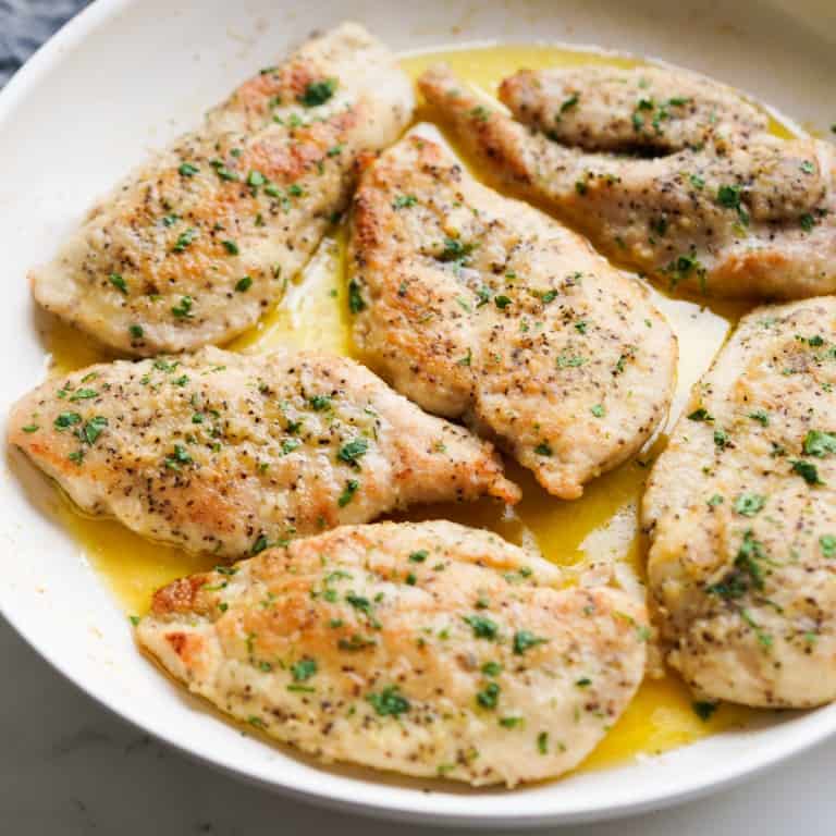 Chicken breast in skillet with garlic butter and topped with parsley
