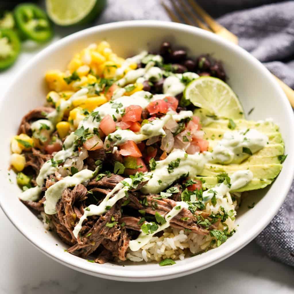 Beef burrito bowl along with corn, pico, avocado and drizzled with avocado crema
