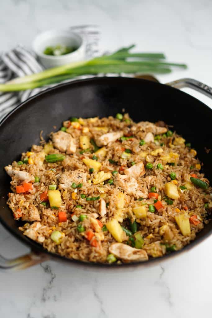 A large wok filled with pineapple fried rice with green onions in the background