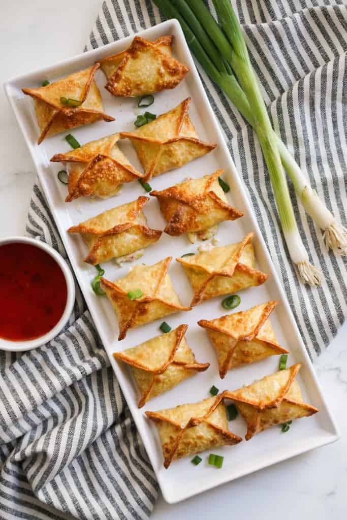 A large rectangular platter of crispy air fryer crab rangoon, with sweet chili sauce on the side for dipping
