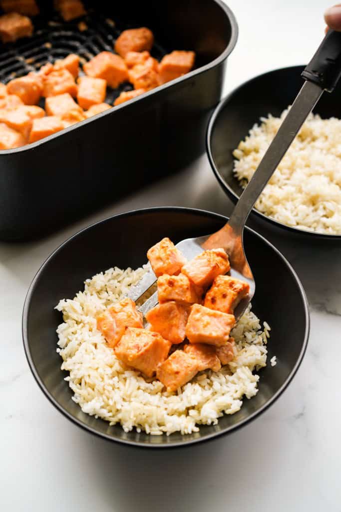 Adding air fryer salmon bites to a bowl filled with rice