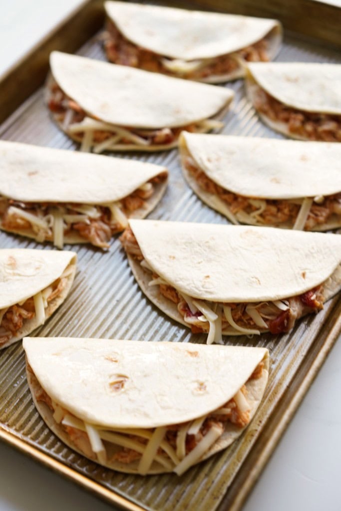 Unbaked chicken tacos with cheese on a baking sheet