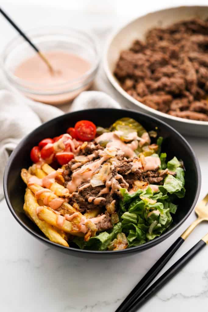 Burger in bowl form with sauce and a skillet of ground beef in the background.