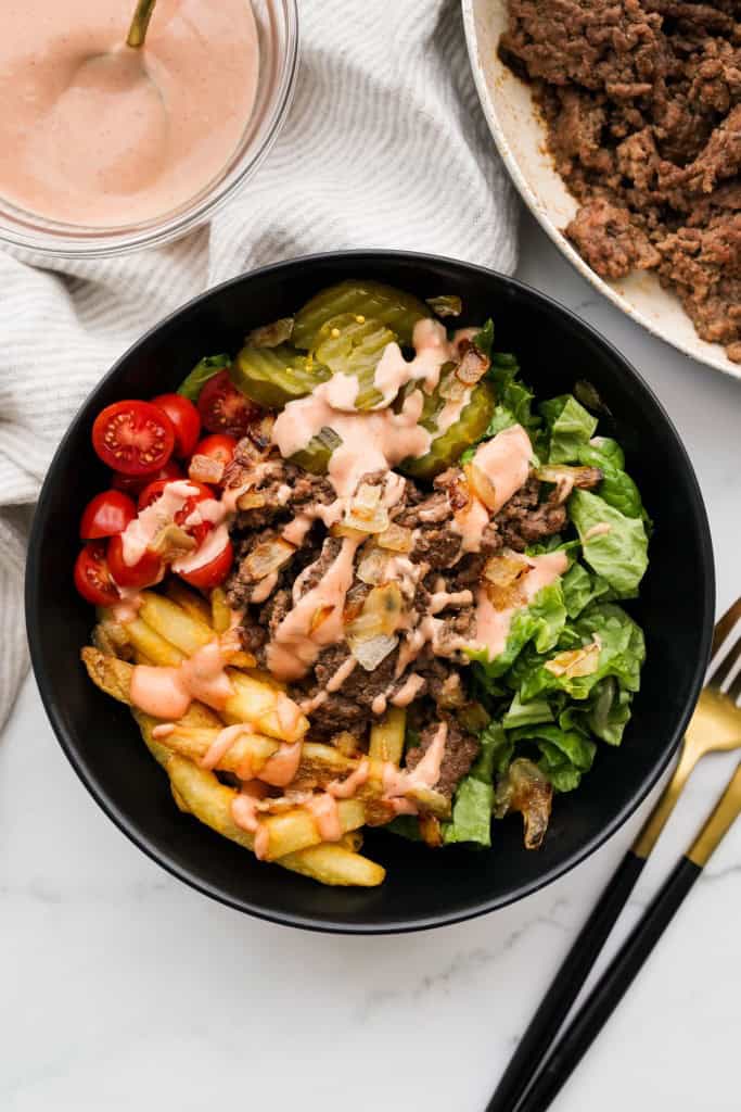 Top down view of a burger bowl loaded with fries, ground beef, lettuce, tomatoes, pickles and topped with burger sauce