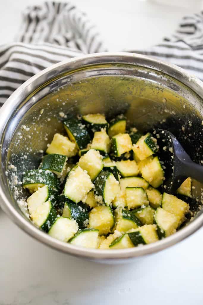 Diced zucchini tossed in garlic parmesan mixture in a mixing bowl