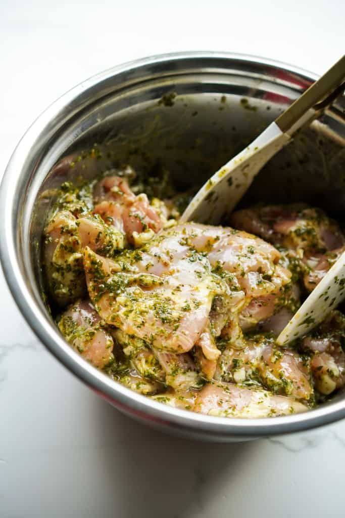 Chicken thighs marinated in chimichurri sauce in a mixing bowl