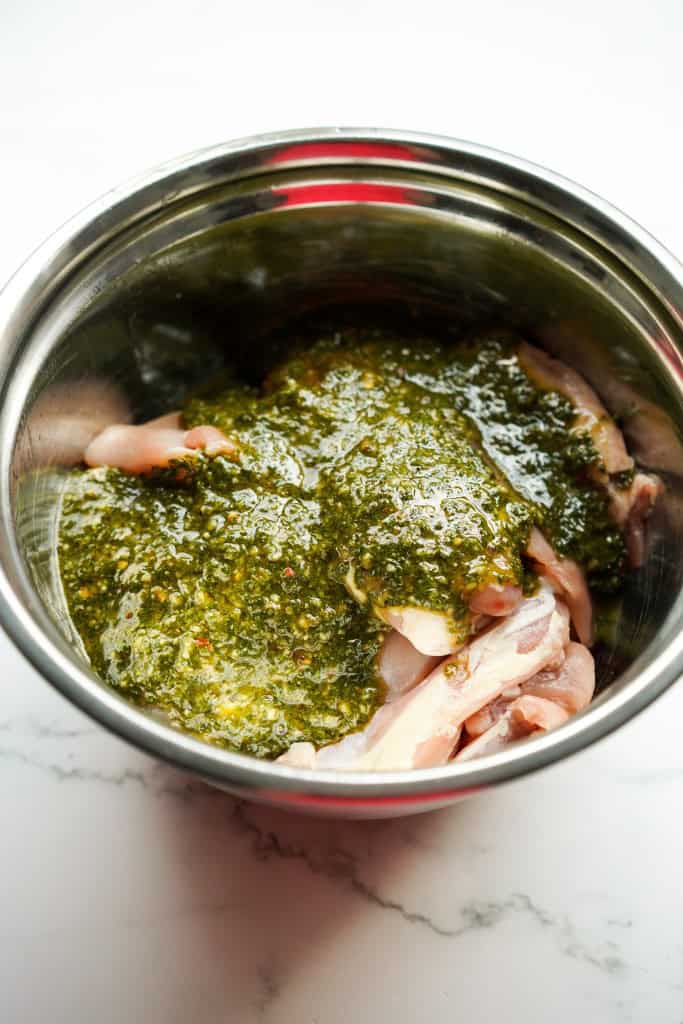 Chimichurri sauce poured over chicken thigh pieces in a mixing bowl