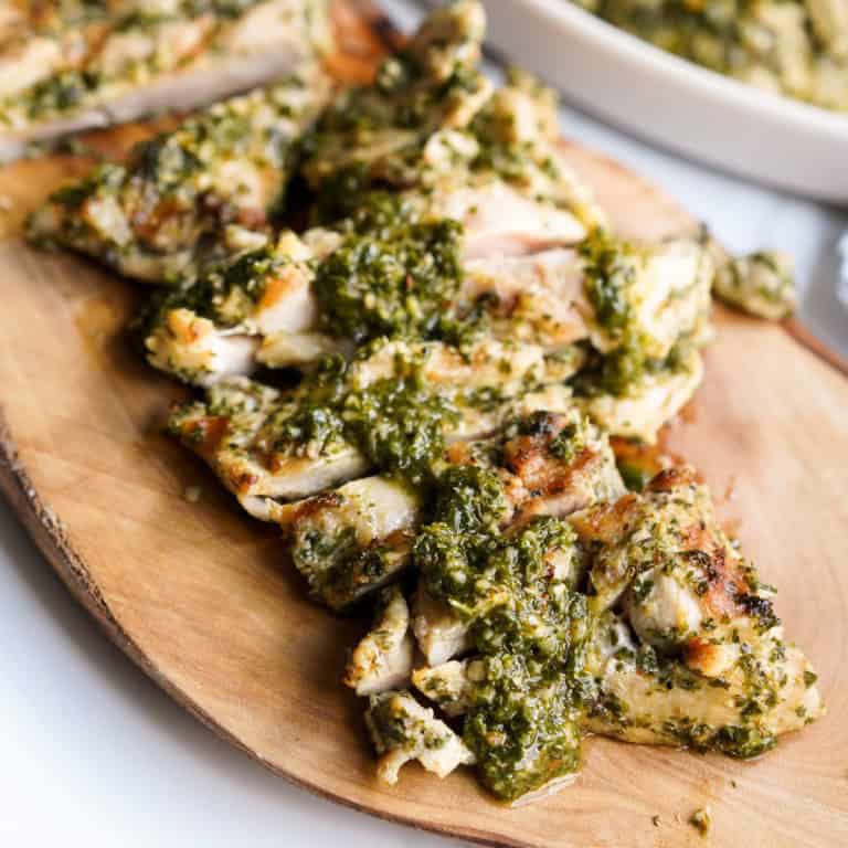 Grilled chimichurri marinated chicken topped with more chimichurri sauce on a wood platter