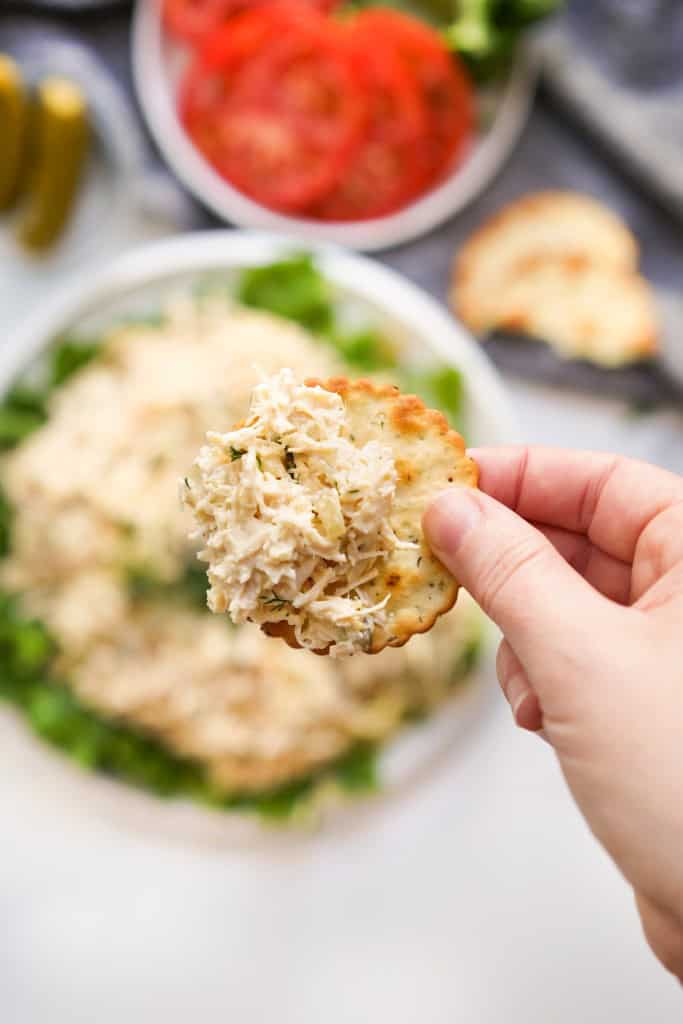 Lifting up a cracker piled with dill pickle chicken salad