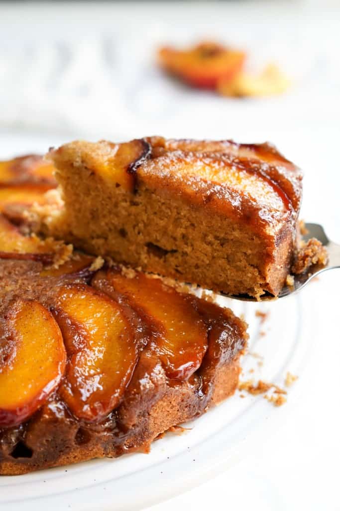 Cutting a slide of cake with sliced peaches and brown sugar glaze topping